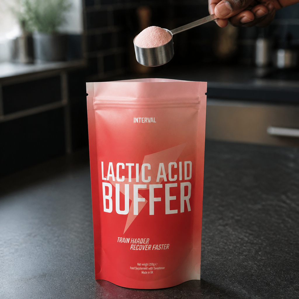 A person's hand holding a metal scoop over a red stand-up pouch labeled 'LACTIC ACID BUFFER' on a dark kitchen countertop.